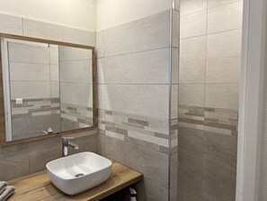 Ein Badezimmer mit einem rechteckigen Waschbecken, einem Spiegel und gefliesten Wänden.