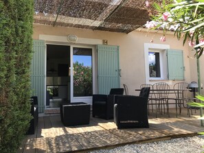 Eine überdachte Terrasse mit Korbmöbeln, einem Grill und Blick auf den Garten.