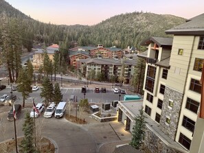 A multi-story building with a stone facade, a parking lot with several cars, and a backdrop of a forested mountain. -  Monache:  Top Floor Larger Studio, Fully Remodeled Studio. Dog Friendly. (Mammoth Lakes)