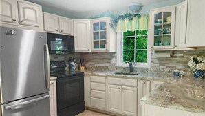 A kitchen with white cabinets, a stainless steel refrigerator, a black oven, and a window with a view of greenery. - Walk to Beach Central AC WiFi Beach Pearl (Chatham)