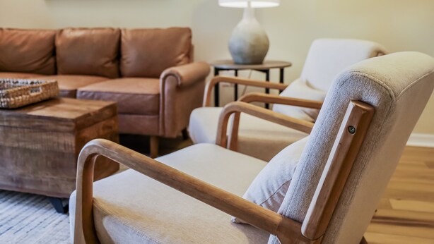 En stue med en brun lædersofa, en hvid lænestol, et træbord og en lampe på et sofabord.