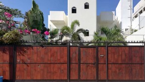 A gated area with a wooden fence, a white building with arched windows, and tropical plants. - Casa Mi Playa (Playa del Carmen)