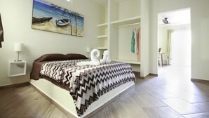 A bedroom with a bed, a painting of a beach scene, a wardrobe, and a view to a dining area. - Casa Mi Playa (Playa del Carmen)