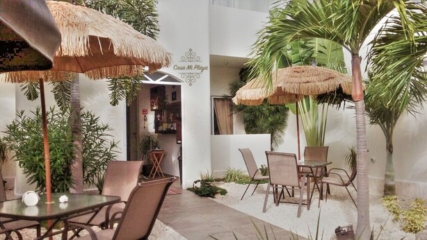 An indoor patio area with thatched umbrellas, palm trees, and seating arrangements. - Casa Mi Playa (Playa del Carmen)