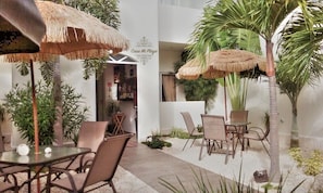 Un patio interior con sombrillas de paja, palmeras y arreglos de asientos.