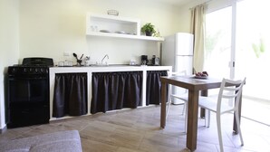 A compact kitchen with a stove, sink, and white cabinets. There is a dining table with chairs and a window with curtains. - Casa Mi Playa (Playa del Carmen)
