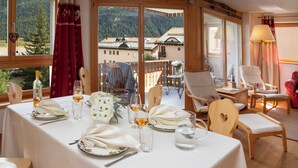 A dining area with a table set for four, a view of a mountain landscape, and a balcony with chairs.