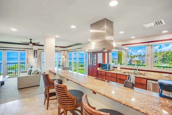 A modern kitchen with a large island, bar stools, and a view of the ocean.