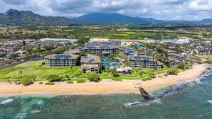 Un complexe hôtelier comprenant plusieurs bâtiments, une plage et un paysage montagneux en arrière-plan.