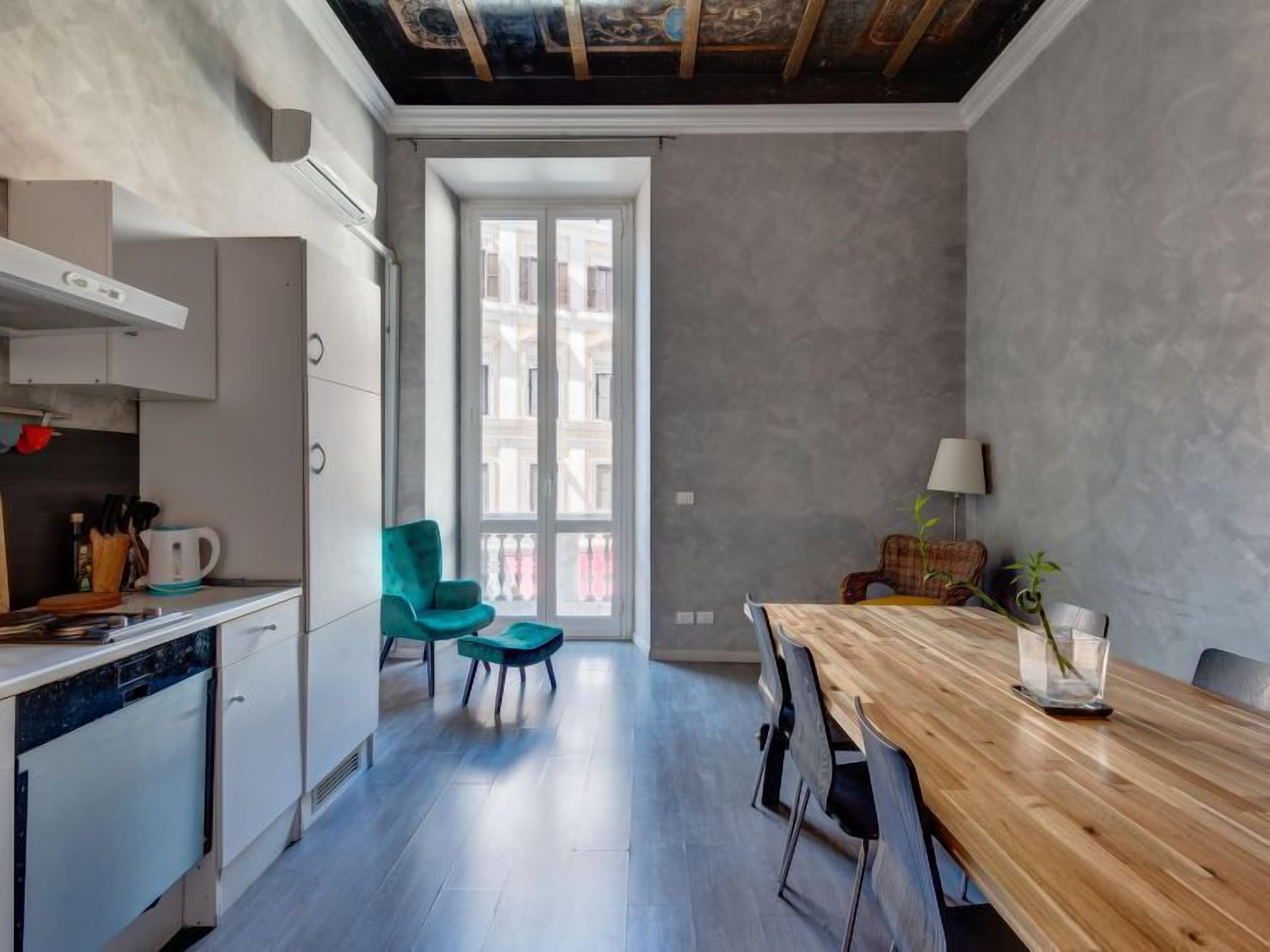 A modern kitchen with white cabinets, a wooden dining table, and a teal chair.