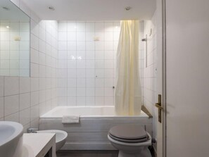 A modern bathroom with white tiles, a bathtub, a toilet, and a sink. - Antico Balcone by Interhome (Rome: Historical City Center)