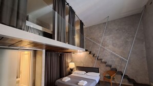 Ett modernt hotellrum med en säng, en stol, en trappa och en dörr som leder till ett annat rum.