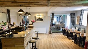 Une pièce spacieuse dotée d’un plancher en bois, d’un coin bar avec des tabourets, d’une table à manger avec des chaises et d’une cheminée.