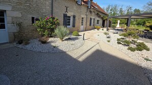 A stone building with a tiled roof, a gravel courtyard, and a pergola.