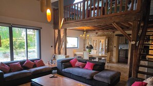 A spacious living area with a high ceiling, a dining table, and a kitchen in the background.