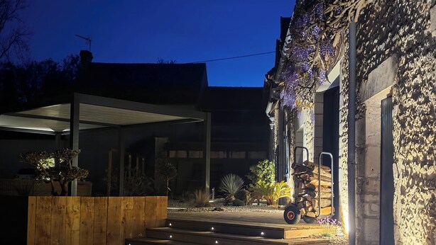A modern house with a wooden deck, a vehicle parked outside, and a stone wall with purple flowers.