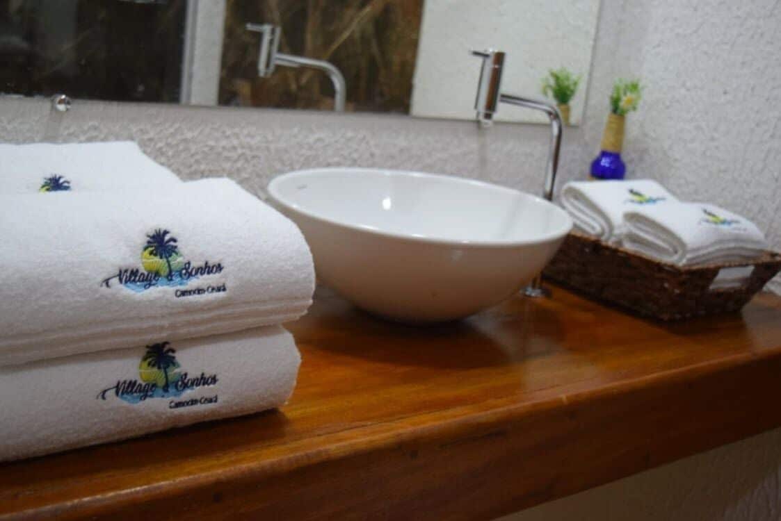 Un baño con un lavamanos blanco, un espejo y toallas con el logo de una palmera.