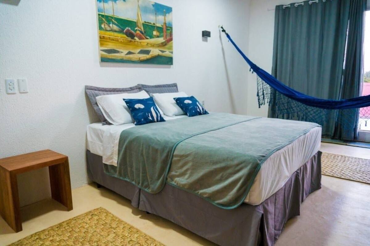 Ein Schlafzimmer mit einem Bett, einem kleinen Holztisch, einer Hängematte und einem Bild an der Wand.