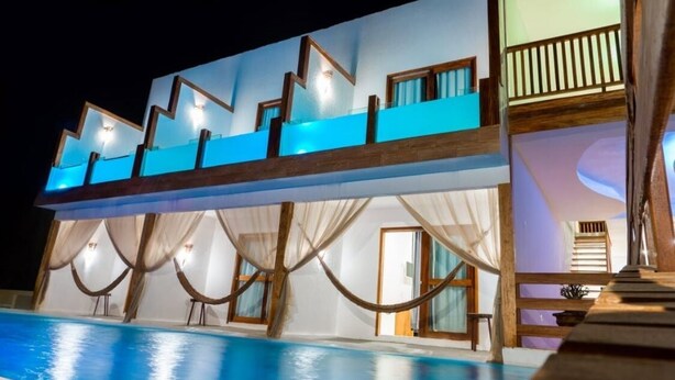 A modern building with a pool, featuring a unique zigzag roof design and a balcony with curtains.