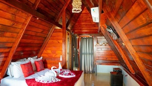 A cozy attic bedroom with a wooden ceiling, a bed with red and white bedding, and a decorative swan centerpiece.