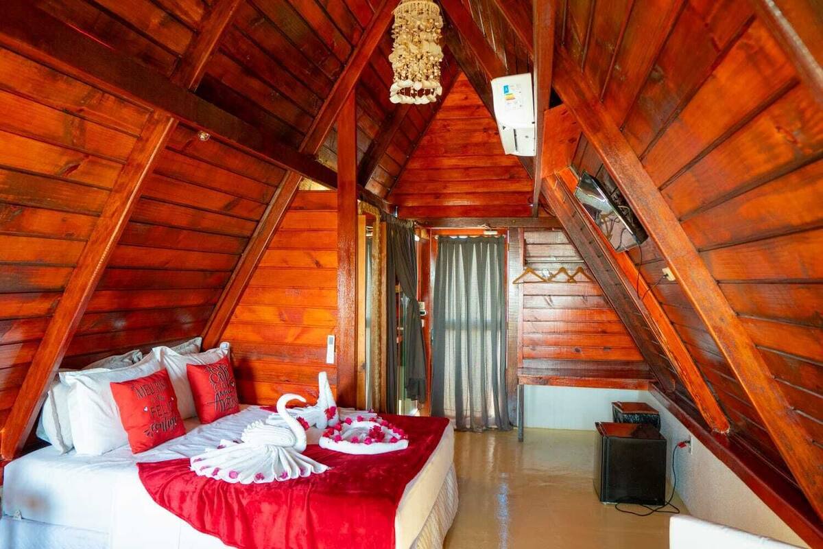 Ein gemütliches Schlafzimmer im Dachgeschoss mit Holzbalkendecke, einem Bett mit rot-weißer Bettwäsche und einer dekorativen Schwane als Mittelpunkt.