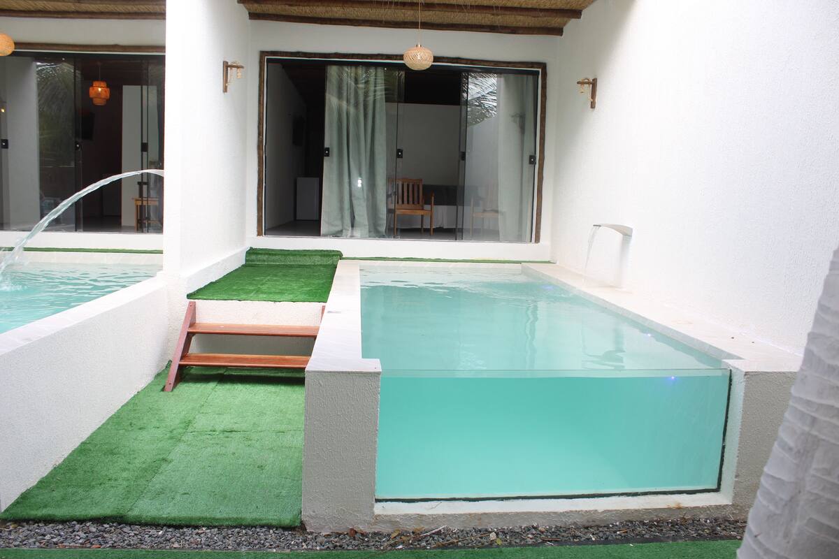 Ein Schwimmbad mit einer kleinen Holzterrasse und einer Glastür zu einem überdachten Bereich.