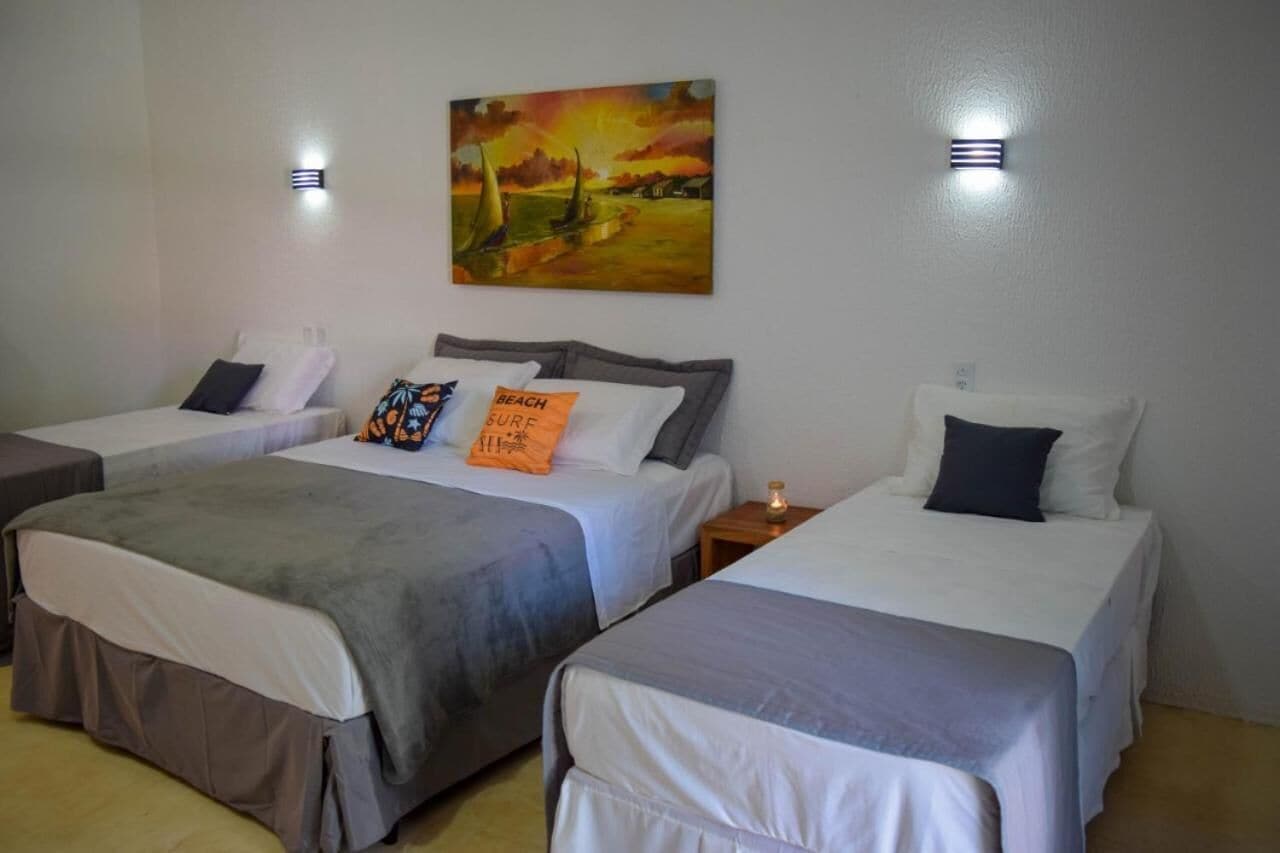 A hotel room with two single beds, a painting of a sunset over a beach, and two wall-mounted lights.