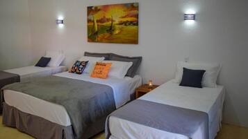 A hotel room with two single beds, a painting of a sunset over a beach, and two wall-mounted lights.