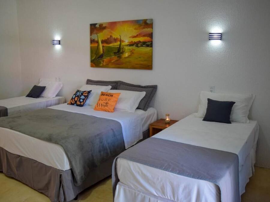 A hotel room with two single beds, a painting of a sunset over a beach, and two wall-mounted lights.