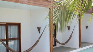 A hammock between two wooden pillars, a pool, and a white wall with windows.