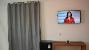 A room with a grey curtain, a black refrigerator, a wooden table with a green candle, and a television on the wall.