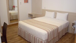 Hotellihuone, jossa on sänky, työpöytä, tuoli, yöpöytä ja peili.
