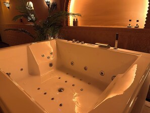 A large, empty bathtub with multiple faucets and a decorative wall behind it.