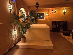 Un hall con mostrador de recepción, plantas en macetas, luces fijadas a la pared y un papel tapiz estampado.