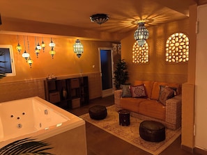 A well-lit living area with a large bathtub, a sofa with cushions, and wall-mounted lighting fixtures.