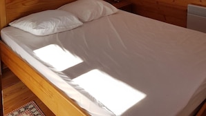 Quarto com painéis de madeira, uma cama, mesa de cabeceira, abajur e janela com vista.