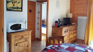 Um quarto aconchegante com um armário de madeira, um micro-ondas, uma televisão e uma toalha de mesa acolchoada.