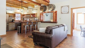 A cozy living room with a leather sofa, wooden flooring, and a kitchen area with bar stools. - Bear Necessities (Vesuvius)