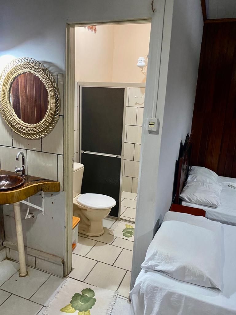 A small, compact room with a wooden vanity, a toilet, and a bed with white bedding.