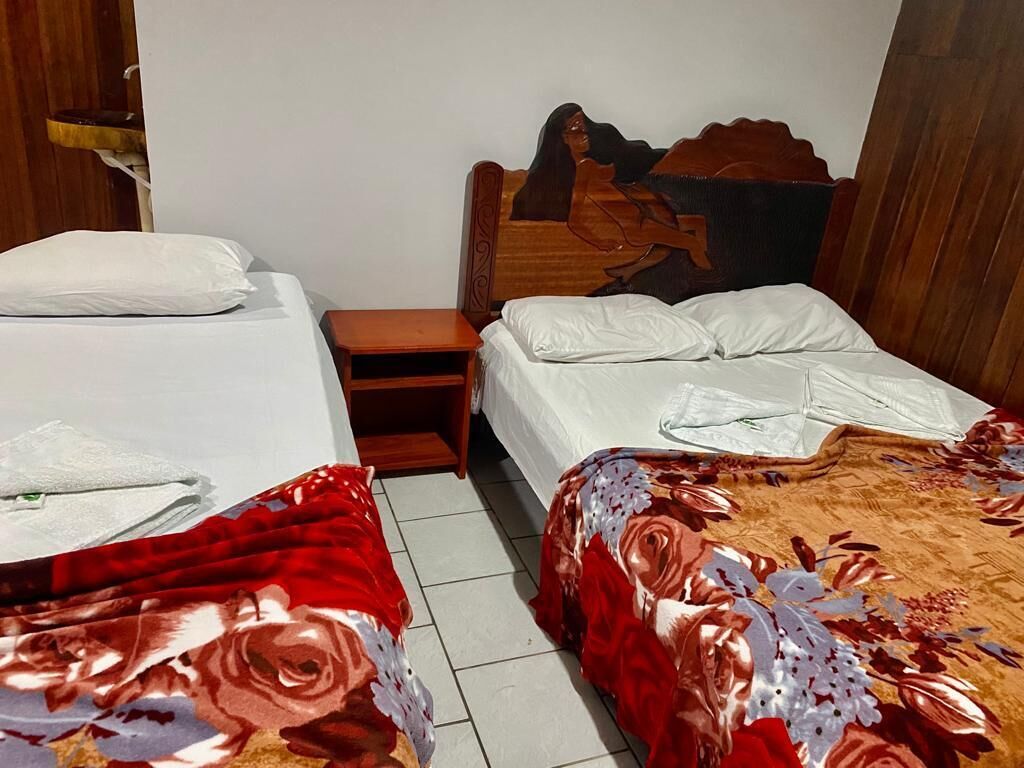 A hotel room with two beds, each with white linens and a wooden headboard. There is a small wooden nightstand between the beds.