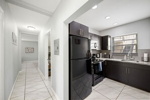A modern kitchen with dark cabinetry, a black refrigerator, and a window with blinds.