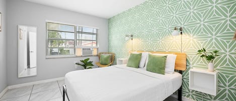 Un dormitorio con cama, ventana, luz empotrada y una planta.