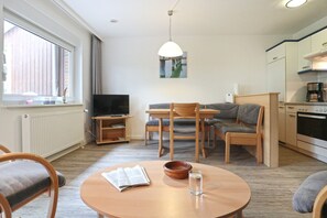 A modern living room with a TV, dining table, chairs, and a kitchen area with appliances.