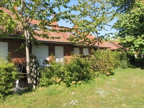 A row of brick houses with red-tiled roofs, surrounded by greenery and a grassy lawn.