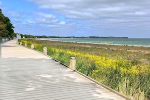 A wooden boardwalk leading to a beach with yellow flowers and a view of the ocean.