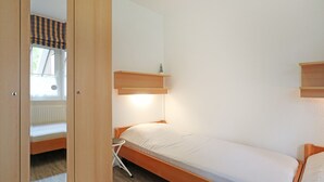 A small, single-bed room with a wooden bed frame, a small bedside table, and a window with a striped blind. - Vacationer village 27c, Germany (Ostseebad Boltenhagen)