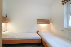 A small, single-room accommodation with two single beds, a window with blinds, and a radiator.