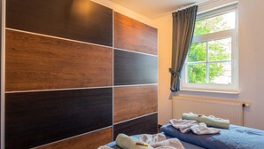 A bedroom with a large wardrobe, two beds with towels, a window with curtains, and a radiator. - Apartment OSTSEELAND 09, Germany (Sellin)