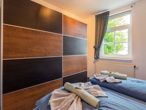 Une chambre dotée d’une grande armoire, de deux lits avec des serviettes, d’une fenêtre avec des rideaux et d’un radiateur.