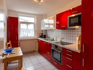 Eine moderne Küche mit roten Schränken, einer Mikrowelle, einem Backofen und einem Fenster mit Vorhängen.